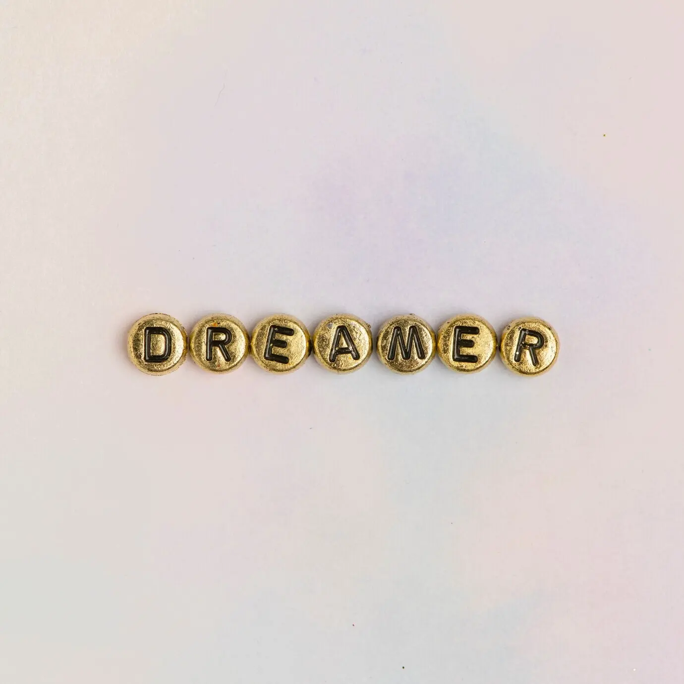 DREAMER in Perlen-Typografie auf pastellfarbenem Hintergrund